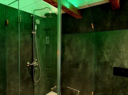 Zu sehen ist eine Eck-Duschwanne, deren Wände vollständig aus Glas bestehen. Die Deckenbeleuchtung sorgt für ein grünes Licht.